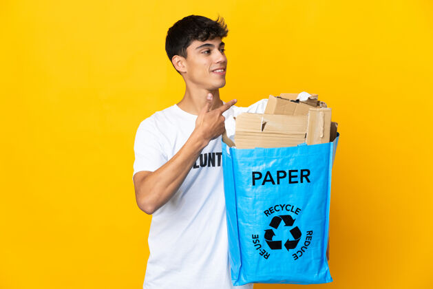 主持人一个男人拿着一个装满废纸的回收袋 翻过一堵黄色的墙 指着后面垃圾积极手指