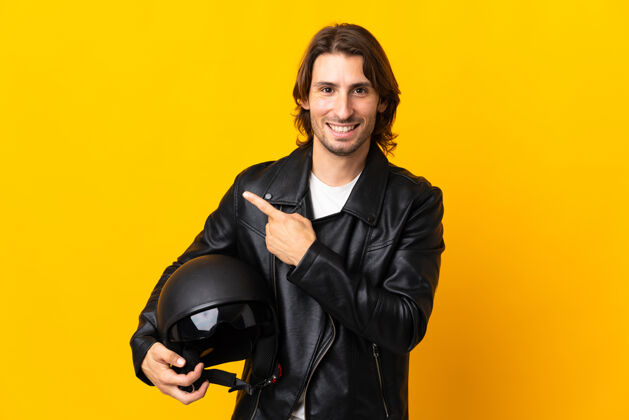 手一个戴着摩托车头盔的男人被隔离在黄色的墙上 指着旁边展示一个产品信心驾驶手指