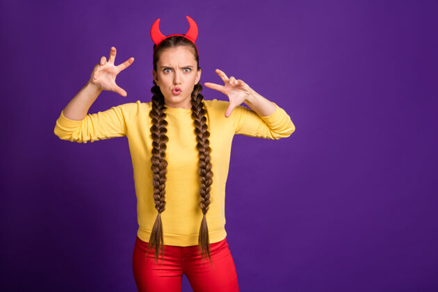化装舞会在Hellowen派对上扮演撒旦角色的少女表情吓人戴喇叭头带休闲黄色套头衫红色裤子隔离紫色墙壁主题乐趣嘉年华