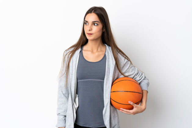 有趣年轻女子打篮球孤立在白色背景看一边年轻积极微笑