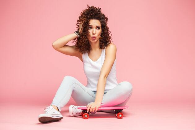 调情快乐迷人的年轻女子坐在粉红色的滑板上乐趣穿衣服