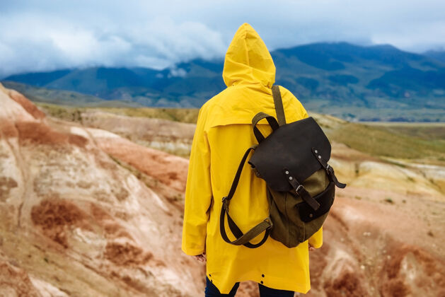 徒步旅行者穿着黄色雨衣背着背包的远足女孩在阿尔泰山脉上旅行者女孩山