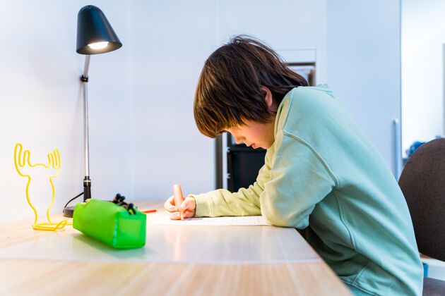 冷静小男孩坐在桌子旁做作业家集中儿童写作家庭教育概念学校知识书桌