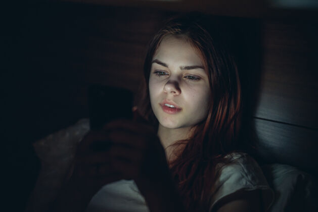 失眠美丽的女人躺在床上 手里拿着一部手机 晚上放松一下在线放松手机