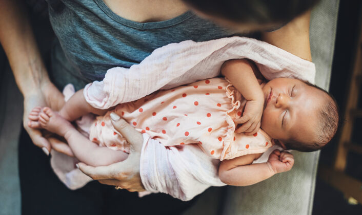 谎言高加索女人抱着他新生的女儿 穿着漂亮的衣服睡在她手里新生儿手宝贝