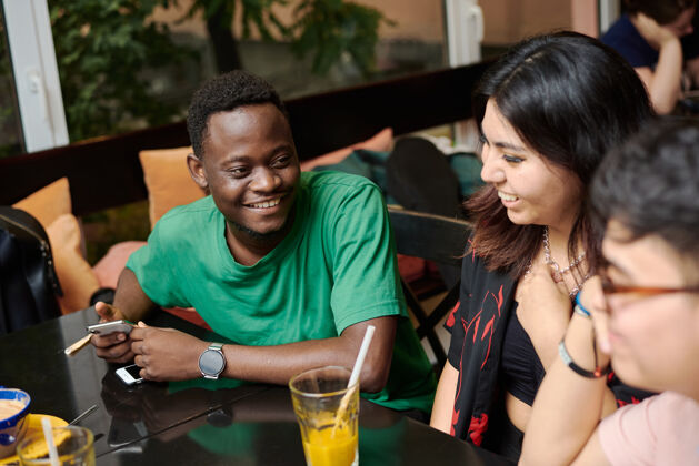 混合在一家现代化的咖啡馆里 一个年轻的黑人男子在朋友的簇拥下和他的女朋友讲笑话交谈微笑成人