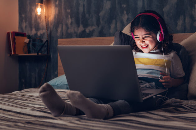 孩子在黑暗中拿着笔记本电脑微笑的小女孩科技观看笔记本电脑