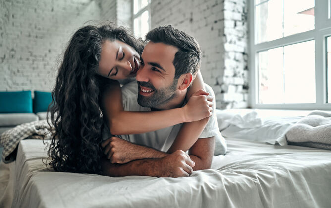 房子早上一起躺在床上的快乐性感的年轻夫妇关系微笑房间