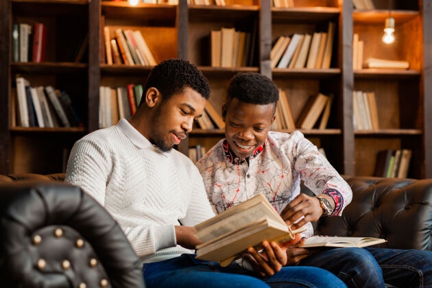 图书馆两个年轻的非洲男人正坐在沙发上看书书非洲文学