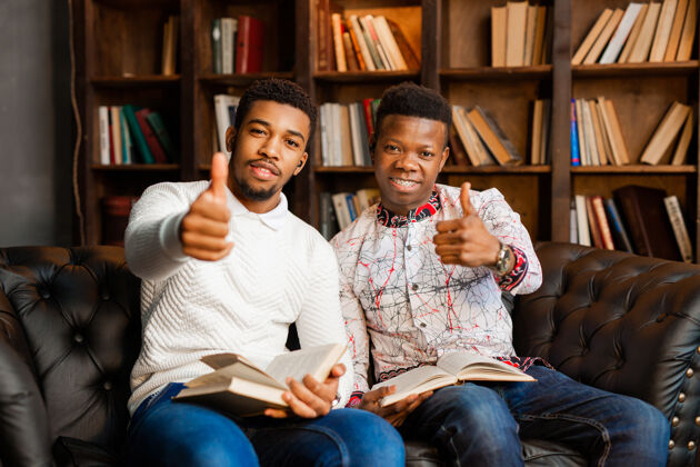 非洲两个年轻的非洲男人坐在沙发上 手拿着书休闲人课堂