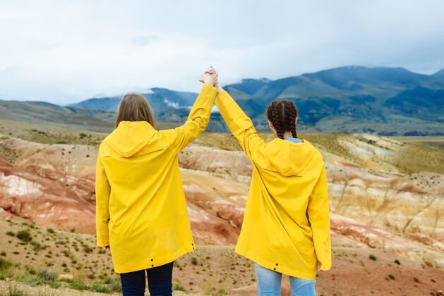 女性两个女人手牵着手走在彩色山脉的背景上户外美丽人