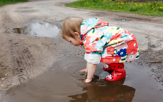 树叶一个穿着鲜艳夹克和胶靴的小女孩在春天快乐地玩耍水坑孩子们我的幸福泥土美丽下雨