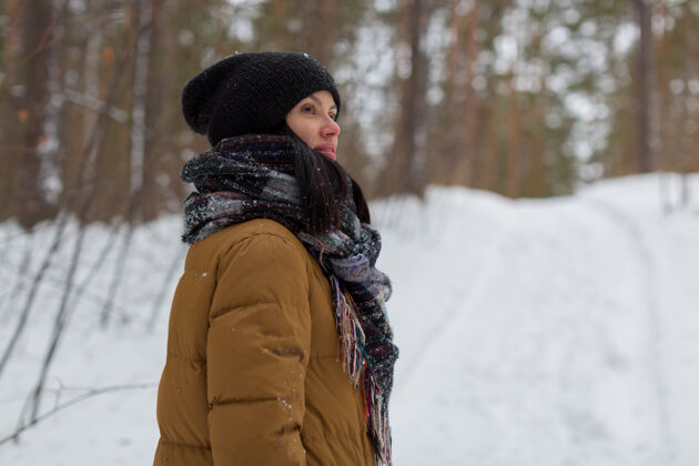 围巾一个戴着黑帽子和棕色夹克的小女孩站在冬天的森林里 遥望远方天气自然寒冷