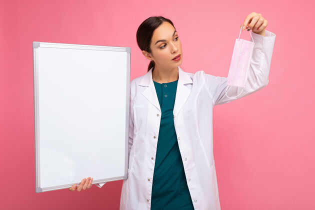 板一名女医生 身穿白色医用外套 手拿空白板 空白板上留有文字和隔离的防护面罩背景.covid概念白板流行病冠状病毒