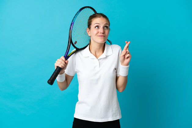 十字架年轻的女子网球运动员 被隔离在蓝色的背景下 手指交叉 祝一切顺利祈祷健康网球