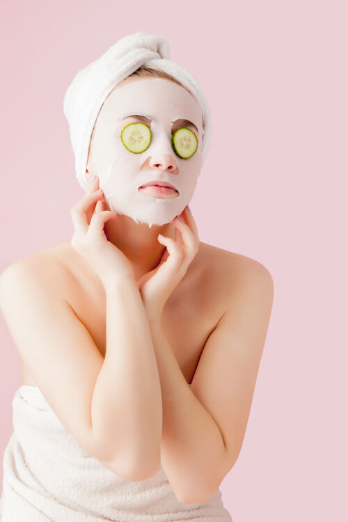 女性美丽的年轻女子正在用化妆纸面膜敷在脸上 黄瓜是粉红色的成人皮肤护理健康