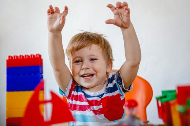 室内一个欢笑的小男孩坐在桌子旁 手里拿着五颜六色的玩具向上向上高质量的照片创意童年建筑工具包
