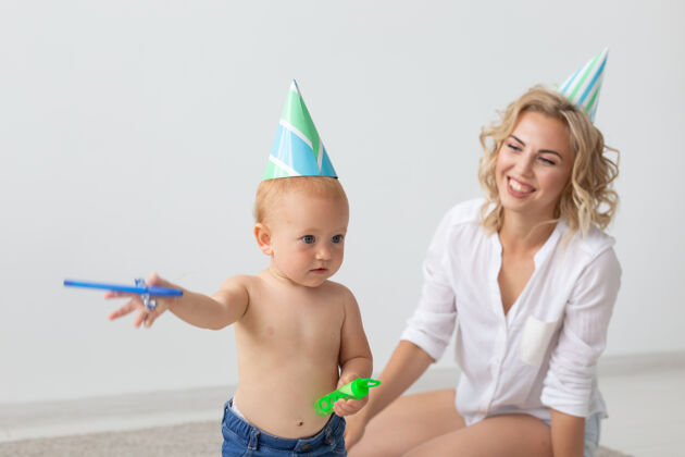 宝贝年轻微笑的母亲和戴着生日帽的可爱的小女儿在家里的地毯上共度时光生日家庭服装