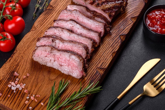 木板新鲜多汁美味的牛排 放在深色烤箱里背景.肉用香料和香草做的菜特写新鲜餐桌