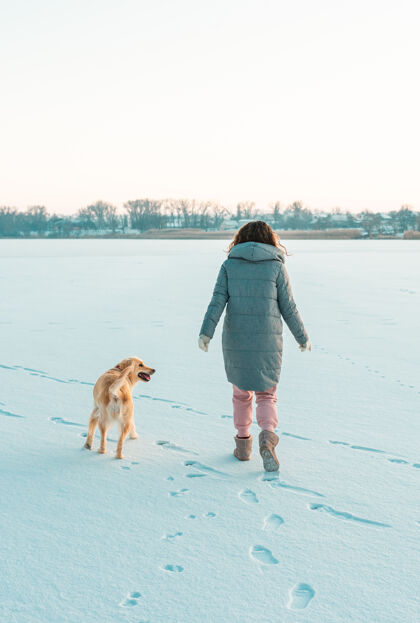 散步冬天散步的年轻漂亮的黑发女子穿着暖和的衣服在雪地里与狗雪地冬天的概念国内宠物公园