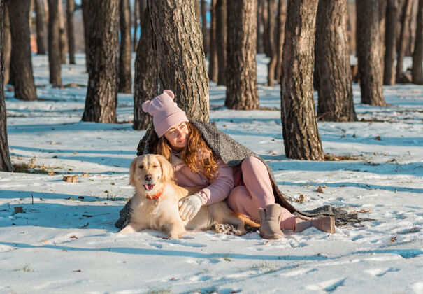 肖像在雪域森林里 一个快乐的女人抱着她的金色猎犬 猎犬身上裹着格子呢休闲狗女孩