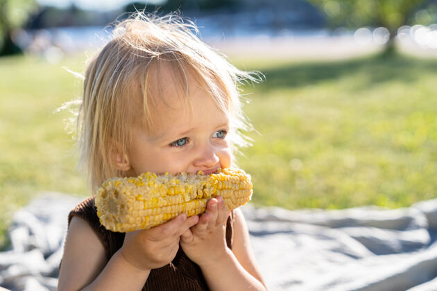 女孩小女孩吃甜玉米芯 夏天坐在草地上白天健康吃东西小吃新鲜草