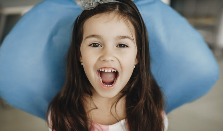生活方式一个可爱的小女孩坐在口腔科的座位上看摄像机的特写照片 展示了一个儿科口腔科的牙齿手术后的牙齿口腔美丽卫生