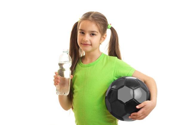 肖像可爱的小女人手里拿着足球 在白色的瓶子里喝水可爱人球迷