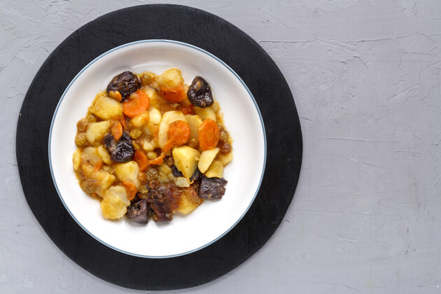 甜一道犹太料理甜甜的tsimes 胡萝卜和红枣 素食者放在一个盘子里 放在混凝土表面的圆形支架上干果土豆胡萝卜