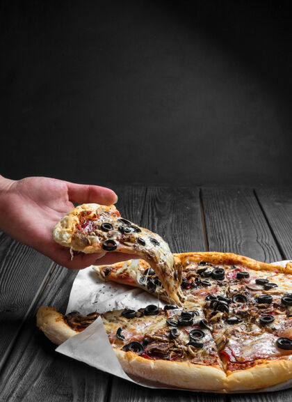 地壳传统的意大利披萨在黑木板上 手里拿着一块披萨 番茄比萨饼黑橄榄