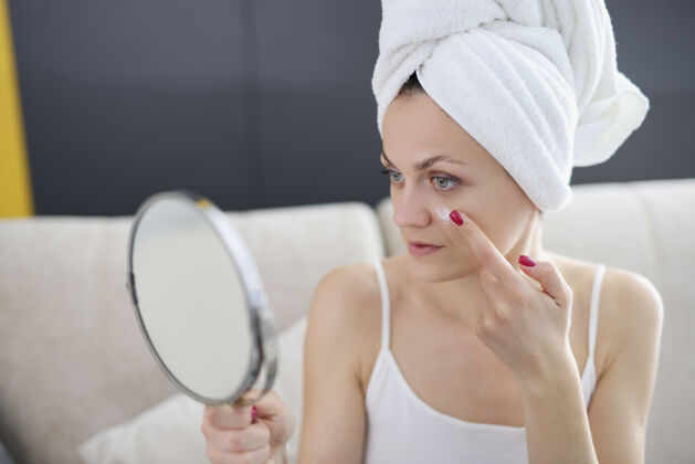 例行年轻女子手里拿着镜子 脸上涂着面霜浴室.每天皮肤护理洗澡保湿成熟