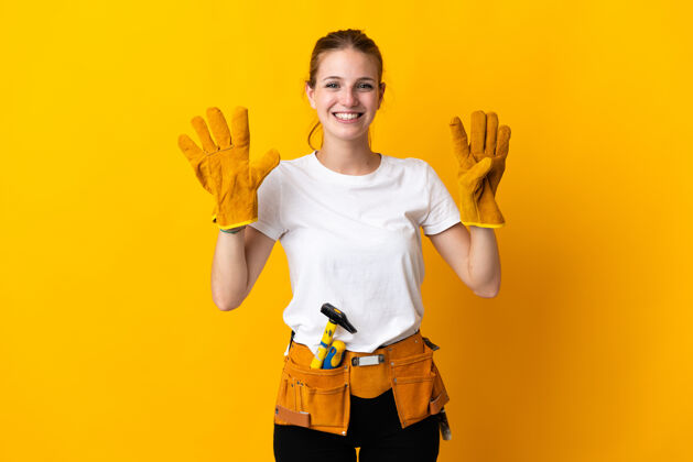 手工被隔离在黄色背景上的年轻电工女人用手指数着九工人数字木工
