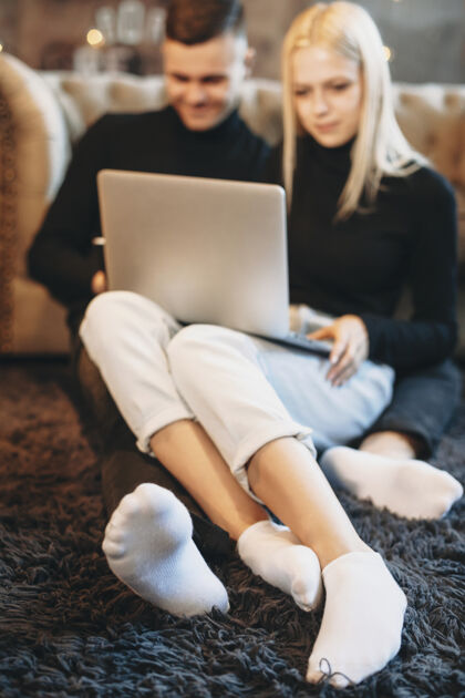 女朋友一对年轻夫妇坐在地板上 靠在沙发上 在家里一起用笔记本电脑金发移动搬迁