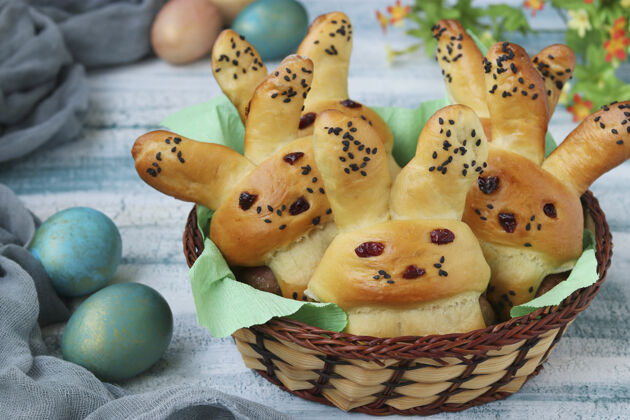 圣诞节复活节小面包以野兔和五颜六色的鸡蛋的形式放在一个蓝色表面的柳条篮子里 这是给孩子们的烹饪创意 特写小吃食物菜单