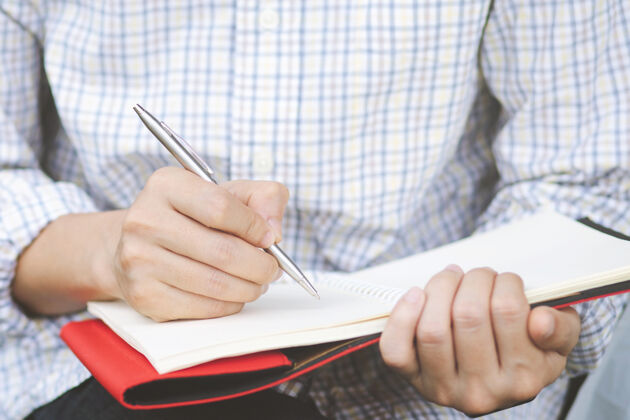 页面年轻人手里拿着用蓝色铅笔打开的笔记本 放在带书签的木质桌子上桌面铅笔书籍