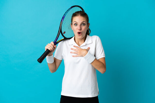 休闲被隔离在蓝色背景上的年轻女子网球运动员在向右看时感到惊讶和震惊惊喜运动员嘴巴