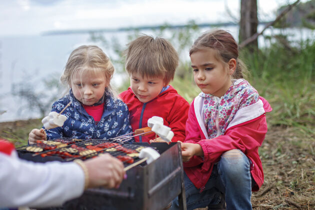 烧烤一群孩子坐在火炉旁 准备在营火上烤棉花糖糖 周末徒步旅行 在当地禁闭后旅行 留宿甜蜜自然篝火