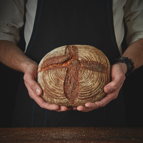 面包房一个男人拿着一个圆形黑面包的手的特写镜头无麸质新鲜面包