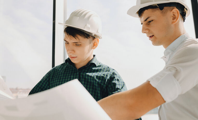 建筑两个戴着头盔的白种人在一张大纸上规划一座建筑办公桌技术工作