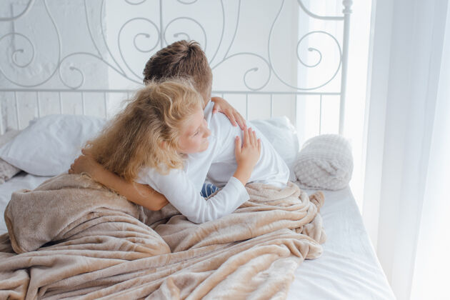 早晨两个孩子男孩和女孩在床上拥抱在早上 兄弟姐妹舒适睡眠儿子