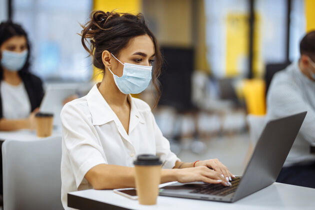问候语一位妇女在办公桌上用笔记本电脑工作 戴着医用口罩 在covid-19大流行期间保持安全医疗隔离男性