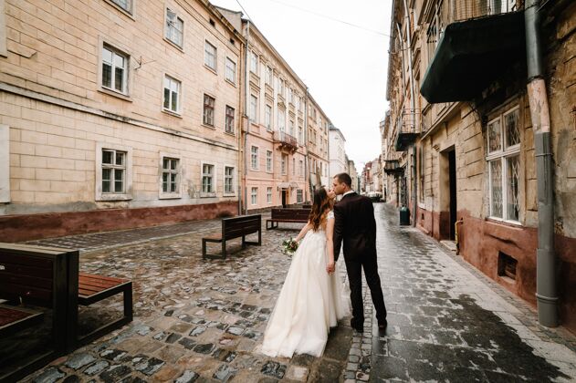 女孩想象一下新郎和新娘在老房子外面的老房子附近亲吻 户外新婚夫妇走在城市的街道上lviv.婚礼走旧爱情男人