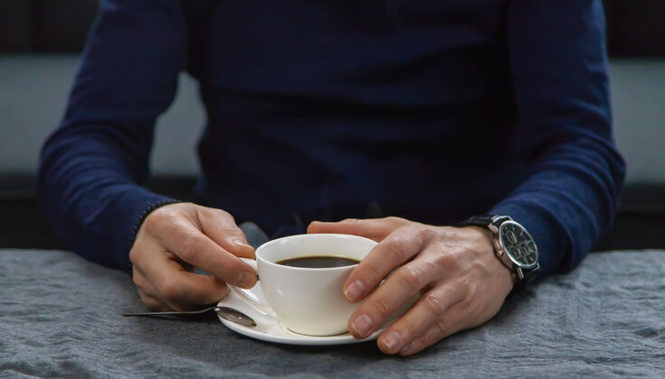 咖啡馆一个男人端着一杯咖啡坐在桌边学生城市餐厅