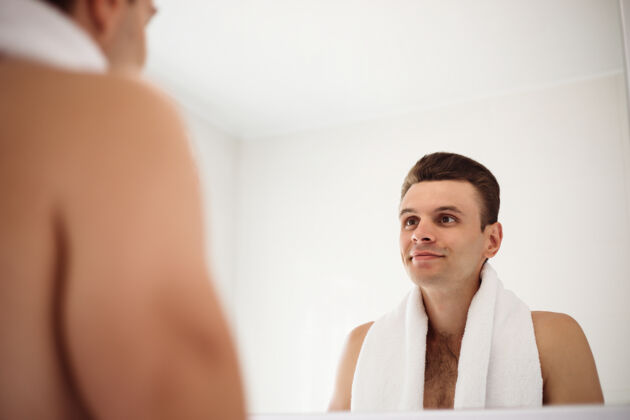 治疗英俊的年轻人在街上刮胡子浴室.肖像一个时髦的裸体胡须男人在家里的镜子里检查他的脸反射仪式修剪