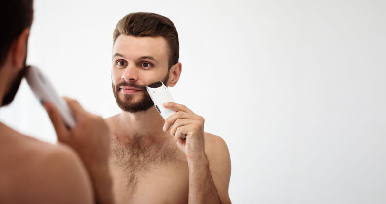 肌肉英俊的年轻人在街上刮胡子浴室.肖像一个时髦的裸体胡须男人在家里的镜子里检查他的脸剃须刀剃须皮肤