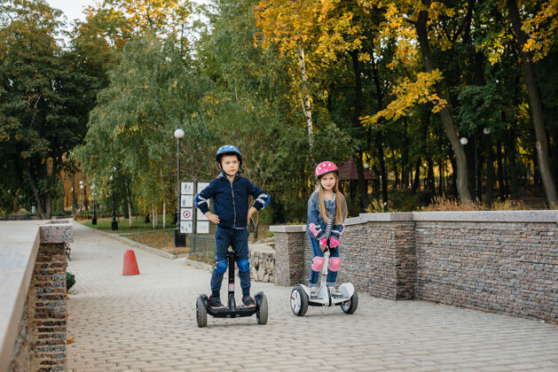 户外快乐的男孩和女孩骑赛格韦在公园里在温暖的秋日日落城市环保乐趣