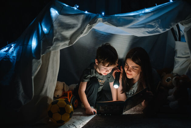 女儿幸福家庭母子俩在帐篷里用手电筒看书主页.家庭概念女孩夜晚魔术