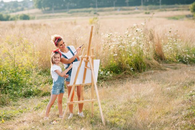 绘画家庭 孩子和人的概念-快乐的母亲和女儿在绿色的表面上画画和交谈生物孩子绘画