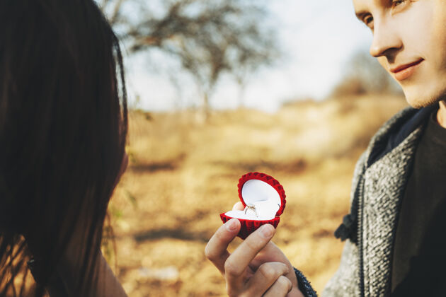 无脸一个帅哥拿着一个盒子 戴着一枚精致的订婚戒指 在阳光明媚的日子里向一个无法辨认的女人求婚快乐女朋友户外