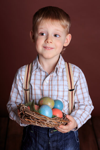 五颜六色一个沉思的小男孩的肖像 手里拿着一个柳条窝和复活节复活节彩蛋概念男孩复活节可爱